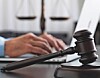 A gavel on a desk with a person typing on a laptop in the background.