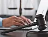 A gavel on a desk with a person typing on a laptop in the background.