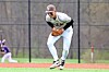 Baseball player in white uniform crouches to field a ground ball on the infield.
