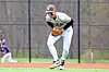 Baseball player in white uniform crouches to field a ground ball on the infield.