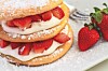 Layered strawberry dessert with cream and powdered sugar on a white plate.
