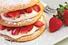 Layered strawberry dessert with cream and powdered sugar on a white plate.