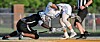 Lacrosse players in black and white uniforms crouch and reach for a loose ball on the field.