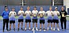 A sports team stands in a line indoors holding certificates and award plaques.