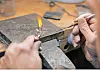 Hands using a small flame tool to heat a metal rod on a worn workbench.