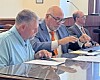 Three men seated at a conference table reviewing documents in a meeting room.