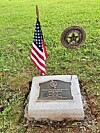 Memorial plaque with an American flag and U.S. Army emblem marker on a grassy patch.