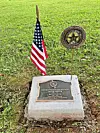 Memorial plaque with an American flag and U.S. Army emblem marker on a grassy patch.