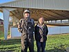 Two people standing on grass in front of an open-sided barn with a metal roof.
