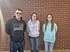 Three people standing together in front of a brick wall.