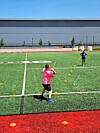 A person in a pink shirt swings a bat on an artificial-turf field during practice.