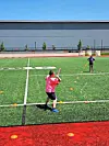 A person in a pink shirt swings a bat on an artificial-turf field during practice.