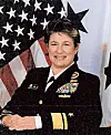 A uniformed military officer poses before an American flag backdrop.