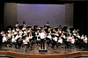 A large school orchestra performs on stage with a conductor at center.