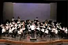 A large school orchestra performs on stage with a conductor at center.