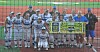 Youth baseball players and coaches pose on a baseball field behind a yellow sign.