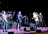 A band performs on stage with microphones, drums and stage monitors.