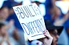 Hand holding a handwritten sign that says “Built to be different” in front of a blurred crowd.