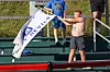 Boy holding a white New Jersey Devils flag beside stadium seating at an outdoor baseball field.