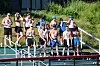 A group of runners in athletic gear stands on a track with numbered bibs and blue caps.