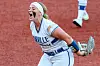 A Virginia Tech softball player in uniform celebrates on a red field.