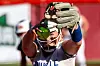 Softball player reaching overhead with a glove and ball in view during a game.