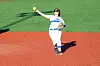 Softball player in white and blue uniform throwing a pitch on the infield.
