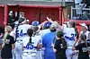 Softball players and coaches stand together near a fence at the field.