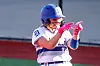 Softball player wearing a blue helmet and pink gloves points with both hands during play.