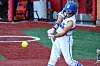 Softball player in white and blue uniform swings at a yellow ball on an artificial turf field.