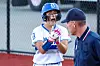 Softball player in a helmet talks with a coach beside the field.