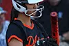 A young softball player wearing a helmet holds a red bat while standing at bat.