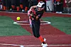 Softball player in black and orange uniform swings at a yellow ball on a turf field.