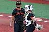 Two softball players in black and orange uniforms stand on a softball field.
