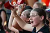 Children with face paint cheering and raising their hands in a crowd.