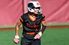 Softball player in a black and orange uniform wearing a white helmet and pink gloves on the field.