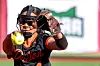 Softball player in black uniform with glove raised to catch a yellow ball.