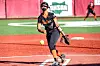 Softball pitcher in black and orange uniform throwing a yellow ball on a turf field.