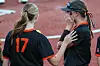 Two softball players in black and orange uniforms standing together on a field.