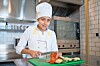 Chef slicing vegetables on a green cutting board in a commercial kitchen.