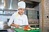 Chef slicing vegetables on a green cutting board in a commercial kitchen.