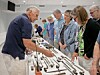 People stand around a table displaying assorted hand tools during an indoor exhibition.