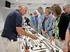 People stand around a table displaying assorted hand tools during an indoor exhibition.