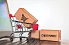 Shopping cart next to a box labeled Cyber Monday on a wooden floor.