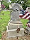 Granite headstone in a cemetery with American flags planted beside it.