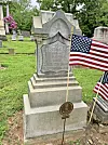 Granite headstone in a cemetery with American flags planted beside it.