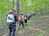 Group of hikers walking along a forest path through trees with backpacks.