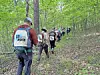 Group of hikers walking along a forest path through trees with backpacks.