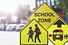 Yellow school zone warning signs with pedestrian and bus symbols beside a street.