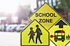 Yellow school zone warning signs with pedestrian and bus symbols beside a street.